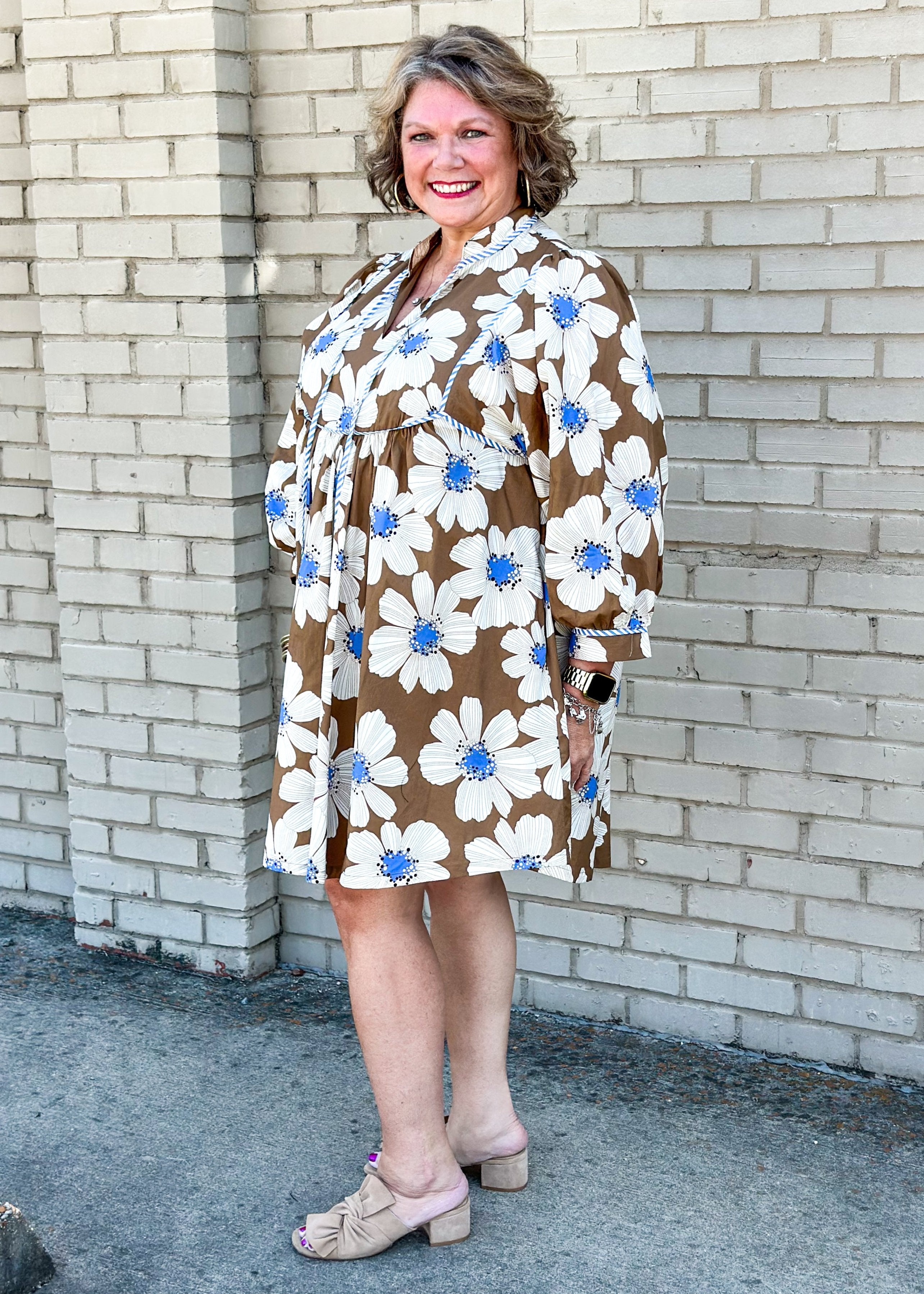 brown base with white flowers and blue centers babydoll dress with pockets and tie neck - blue and white striped piping detail around cuff of 3/4 sleeve and around chest area