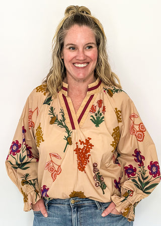 Beige top with v-neckline, contrast trim, and vibrant floral design.