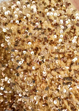 A close-up of a gold sequined fabric with shiny metallic gold, bronze, and silver sequins layered over a textured gold mesh backing.