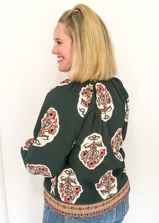 Forest green boho print top featuring smocked collar large floral bundles and colorful border trim.