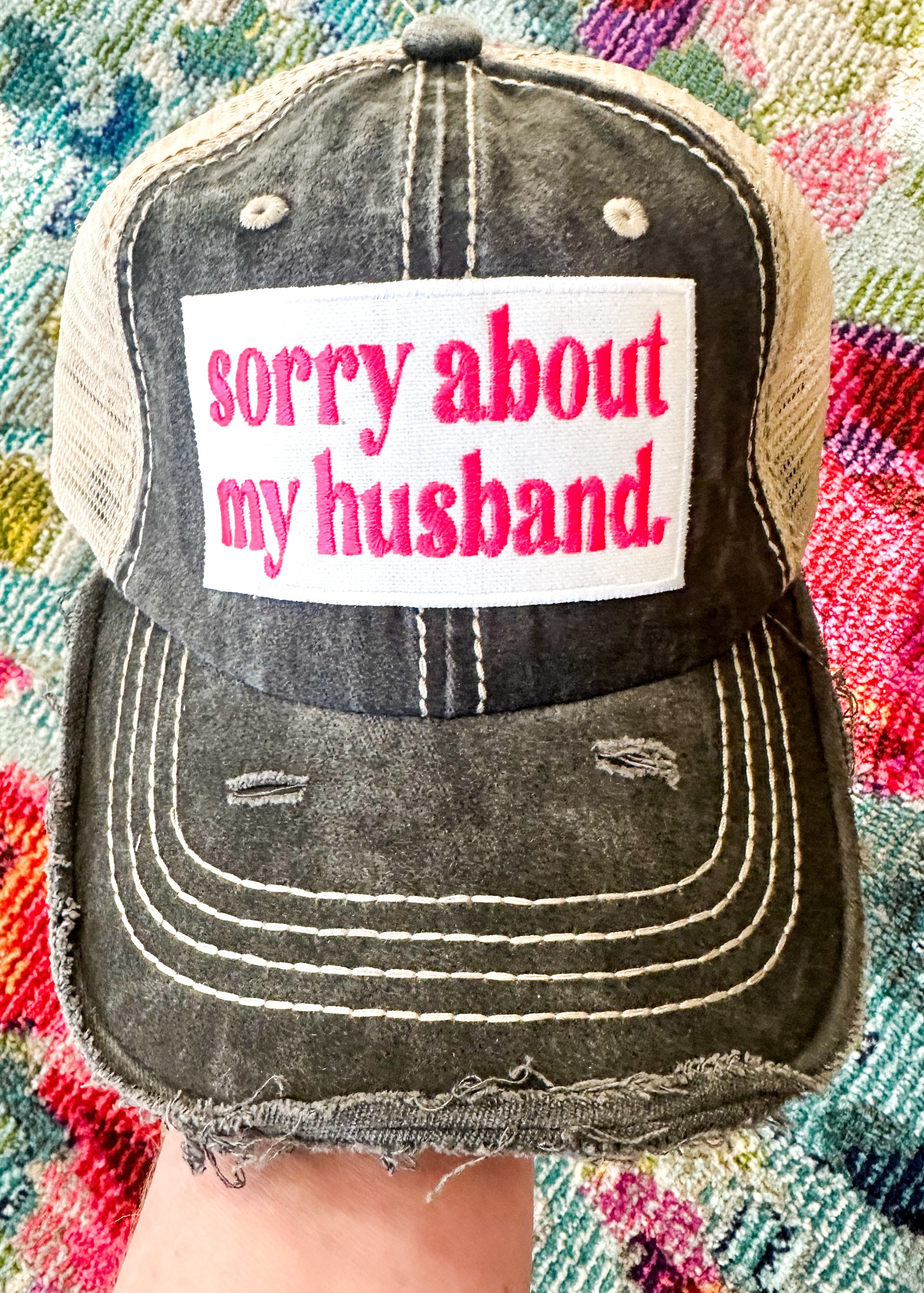 "sorry about my husband" embroidered patch in hot pink on black trucker hat with khaki mesh back.

Velcro closure.