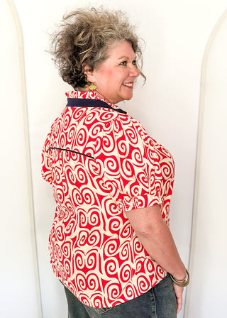 Red swirl print blouse with navy contrast trim, puff sleeves, and split neckline detail.