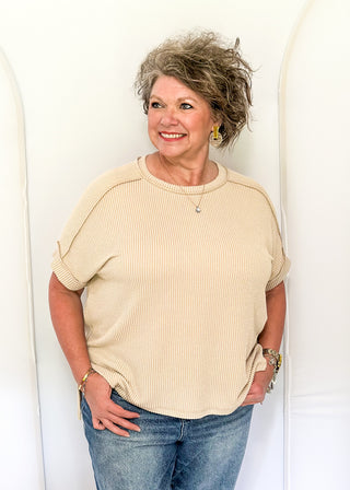 Woman wearing a beige sweater and blue jeans standing against a white background