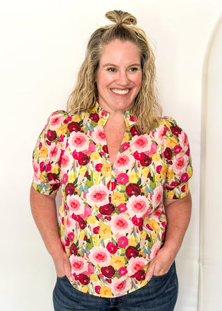 V-neck floral puff sleeve top with bright blooms in pink, wine, gold and green. short sleeve, ruffle collar with 3 button closure. 