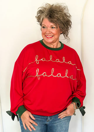 woman wearing a red long sleeve top with Hunter Green contrast, velvet bows on sleeve and sequin lettering "fa La La La la"