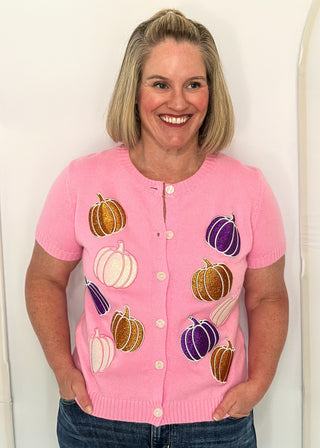 Woman wearing a pink sweater with purple, orange, and light pink glitter pumpkins. 