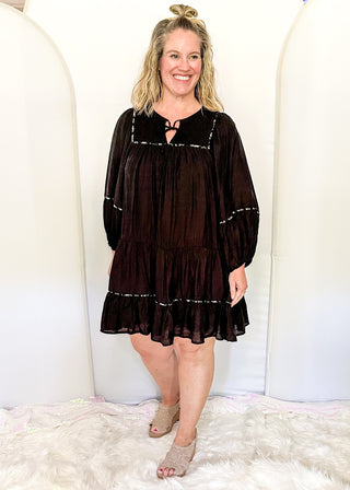 knee length black tiered dress with smocking on the chest and a tie closure at the rounded neck. 3/4 sleeve, leopard piping.
