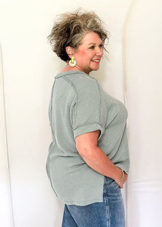 Woman wearing a light green sweater and blue jeans standing against a white background