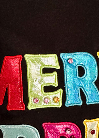 Close-up of colorful embroidered letters on a black fabric background, showing red, light green, and blue letters with small rhinestone embellishments.