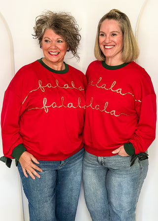 Two women wearing a red long sleeve top with Hunter Green contrast, velvet bows on sleeve and sequin lettering "fa La La La la"
