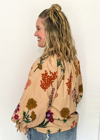 Beige top with v-neckline, contrast trim, and vibrant floral design.
