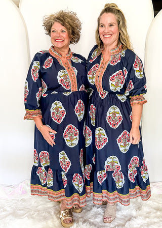 Navy maxi dress with colorful floral medallion print, orange embroidered trim at neckline, and smocked cuffs