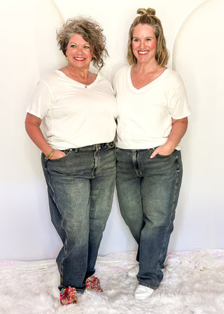 Two women wearing white tops and blue jeans standing against a white background