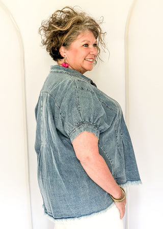 Denim button-down top with short sleeves, pointed collar, vertical stitched panels, and frayed raw-edge hem.