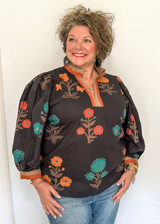 Black floral blouse with colorful flowers, contrast tan and orange trim, and ruffled neckline