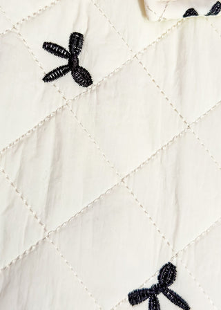 Ivory quilted puffer vest-ruffle sleeve, front pockets, snap closure. Small black bows embroidered throughout.  