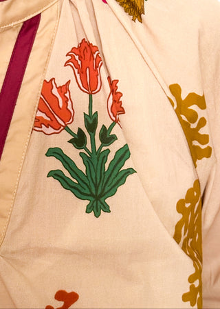 close up of beige top with v-neckline, contrast trim, and vibrant floral design.
