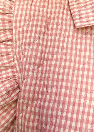 Close-up of a pink and white gingham quilted vest with ruffled sleeves and a pointed collar, worn by a person.