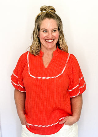 Dark coral short sleeve blouse with puff sleeves, split V-neckline, textured fabric, contrast white stripe trim detailing.