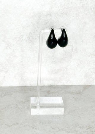 Black earrings on a clear stand against a white background