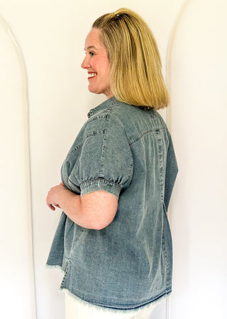 Denim button-down top with short sleeves, pointed collar, vertical stitched panels, and frayed raw-edge hem.