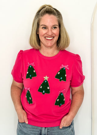 woman wearing a short sleeve pink top with embellished mini trees.