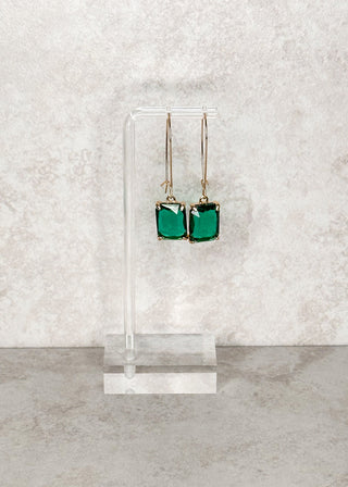 Rectangle gemstone dangle earrings in emerald green. Displayed on a stand 