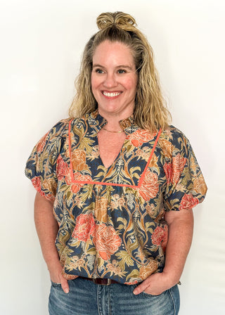 Short puff sleeve navy floral top. Florals are terracotta and coral.  V-neck with coral piping detail on chest.