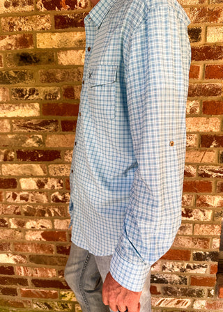 A man wearing a light blue and white gingham long-sleeve button-up shirt, standing in profile against a rustic red-brown brick wall.