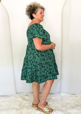 side view of woman wearing Forest green jacquard babydoll dress with square neckline and short sleeves.
