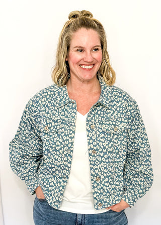 Cropped denim jacket with a blue and white floral print, long sleeves, button-front closure, and chest pockets