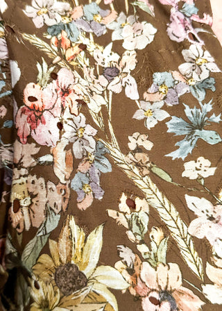 A close-up of a brown fabric with a dense floral and botanical print featuring pink, blue, yellow, and beige flowers and leaves.