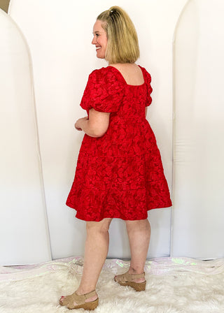 side view of woman wearing red jacquard babydoll dress with square neckline and short sleeves.
