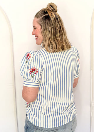 Short sleeve button up top with blue stripes and embroidered floral bundles in red and pink. 