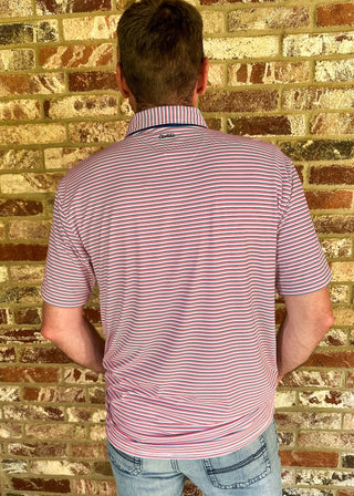 A man viewed from behind wearing a short-sleeve polo shirt with thin red and white horizontal stripes, standing in front of a brick wall.