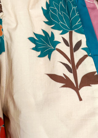 Close up of ecru floral blouse with colorful flowers, contrast turquoise and rose trim, and ruffled neckline