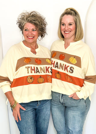 Two women modeling a cream long sleeve top with pumpkins and THANKS in sequins
