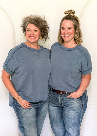 Two women wearing matching blue tops and jeans standing against a white background