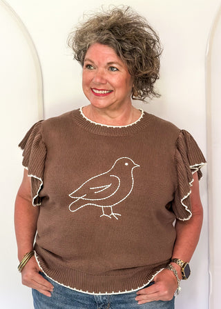 woman wearing brown short sleeve sweater with bird. 