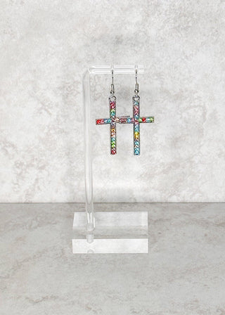 Colorful rhinestone cross fish hook earrings on a clear stand against a light gray marble background