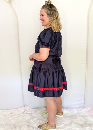 Navy puff sleeve dress with red plaid trim and tiered skirt.