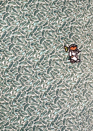 A close-up of a patterned textile or wallpaper featuring a dense, repeating organic design in muted teal, sage green, and off-white. A small cartoon character patch or applique is visible on the right side.