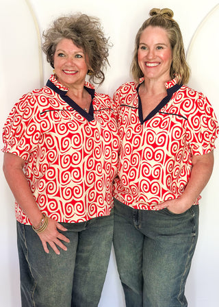Red swirl print blouse with navy contrast trim, puff sleeves, and split neckline detail.