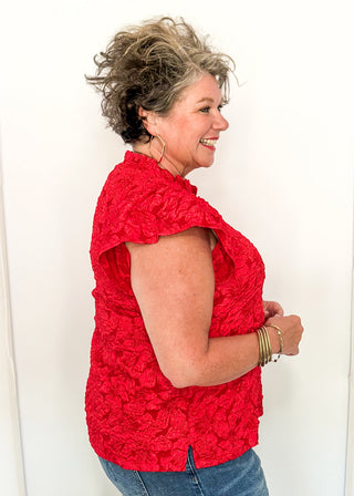 side view of woman wearing red jacquard flutter sleeve blouse with a floral pattern