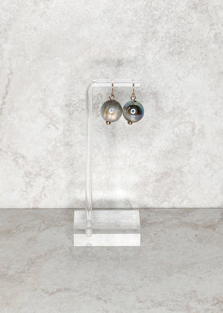 gray bead fish hook Earrings on a clear stand against a marble background