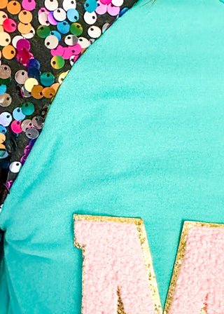 Turquoise long sleeve top with multi color sequin sleeves and chenille ‘MERRY’ lettering across the front.