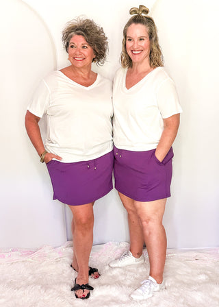Two people wearing the Everyday Skort in purple with white tops.