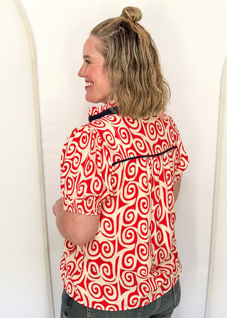 Red swirl print blouse with navy contrast trim, puff sleeves, and split neckline detail.
