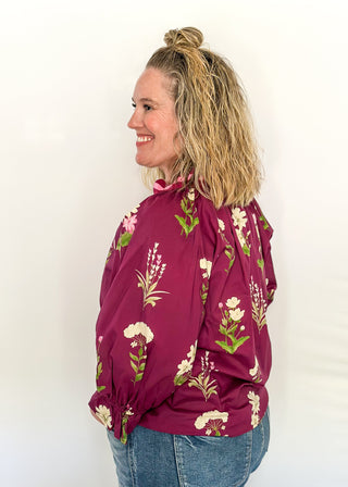 Plum top with florals in light pink and white with green leaves.  3/4 length sleeve and v-neck with contrast detail in plum and light pink. 