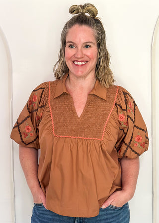 woman in chestnut poplin puff sleeve top with embroidery. 
